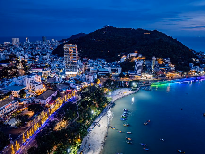 Stunning aerial view of a lively coastal city at night, illuminated by vibrant lights.