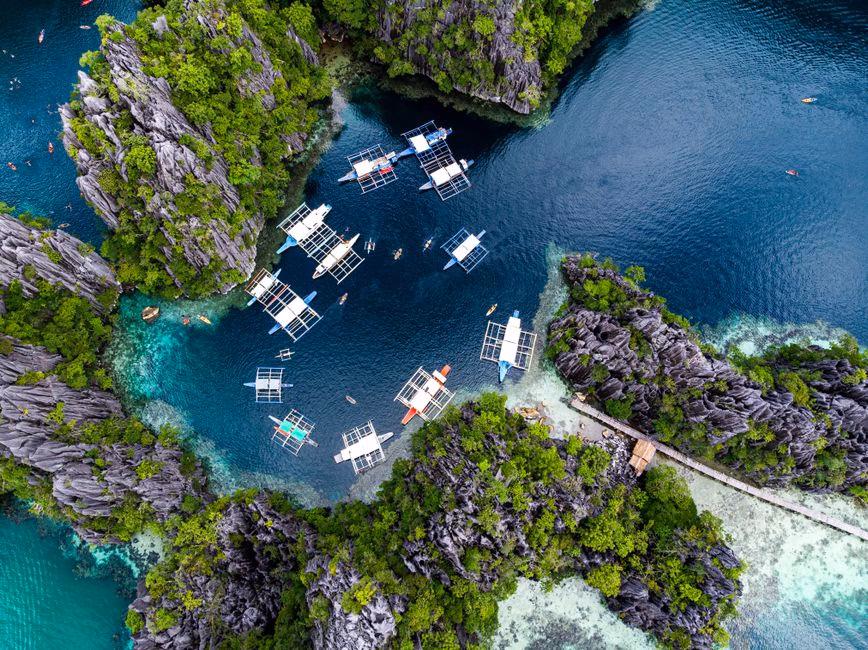 Stunning aerial shot of boats in a turquoise lagoon surrounded by rock formations in El Nido, Palawan, Philippines.