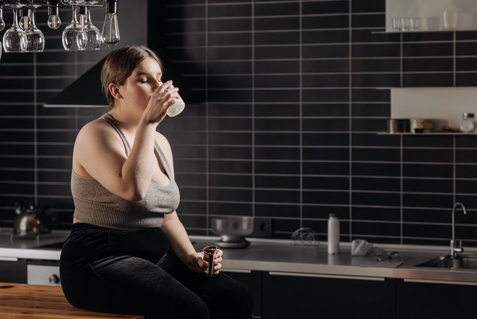 Woman sitting on kitchen counter drinking milk in a modern setting.