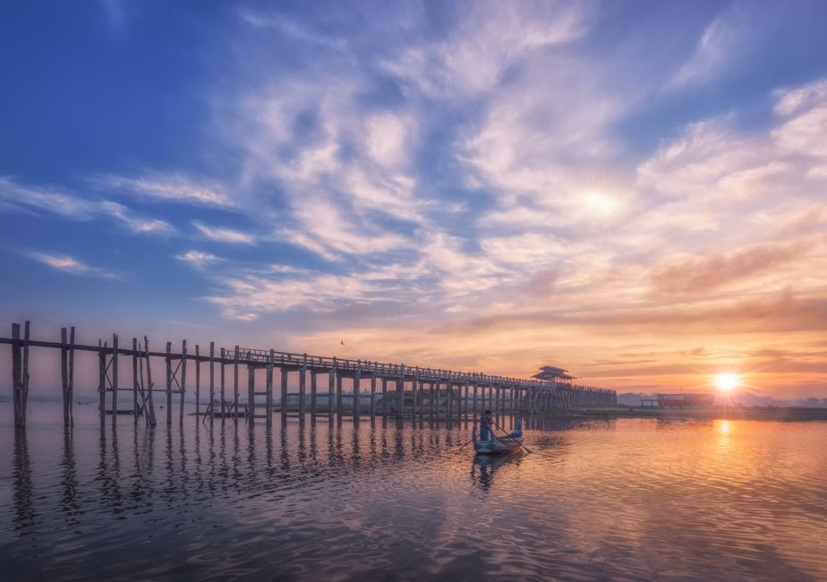 Picturesque sunrise over U Bein Bridge with calm reflective waters and scenic sky.
