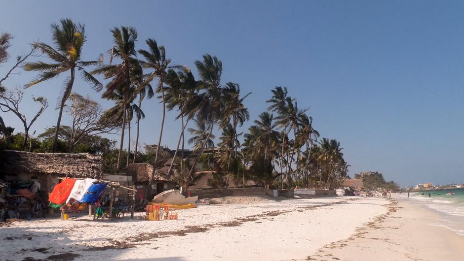 A serene beach with palm trees and bright skies in Mombasa, Kenya.