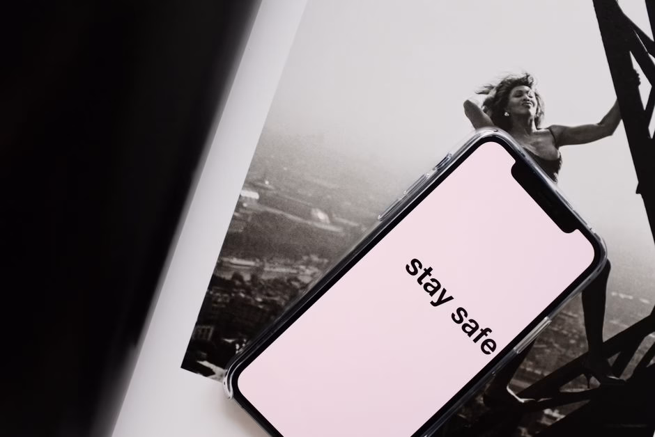 From above of cellphone with pale pink screen and STAY SAFE inscription put on open magazine with image of cheerful female cl