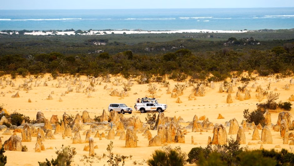 Scenic view of vehicles in the Pinnacles Desert, Western Australia, with ocean in the background.