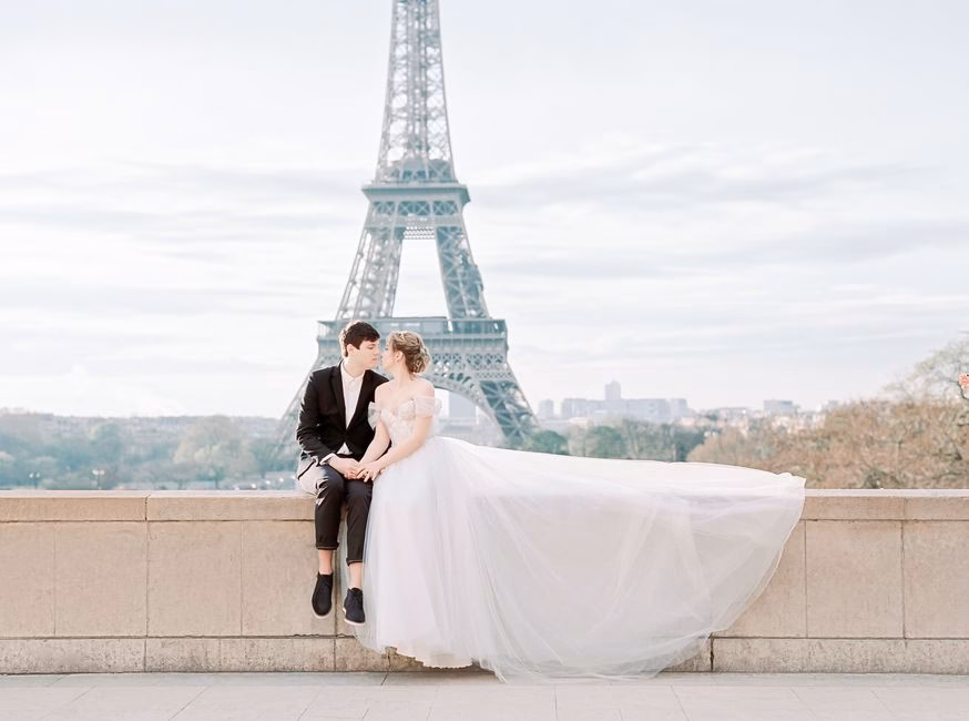 A romantic couple in wedding attire sitting by the Eiffel Tower in Paris, capturing timeless love.