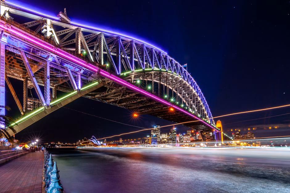 Vibrant lights illuminate Sydney Harbour Bridge against a starry night sky.