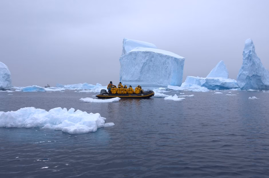 An expedition group in a boat navigating icy waters near giant icebergs in Antarctica.