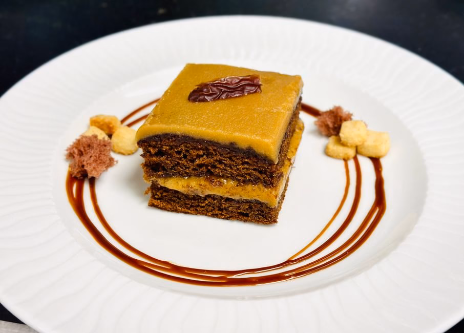 Delicious chocolate cake drizzled with caramel sauce and garnished elegantly on white plate.