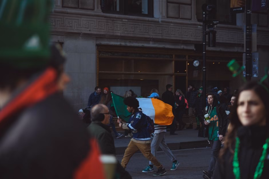 A vibrant street celebration in Chicago with people waving an Irish flag during the day.