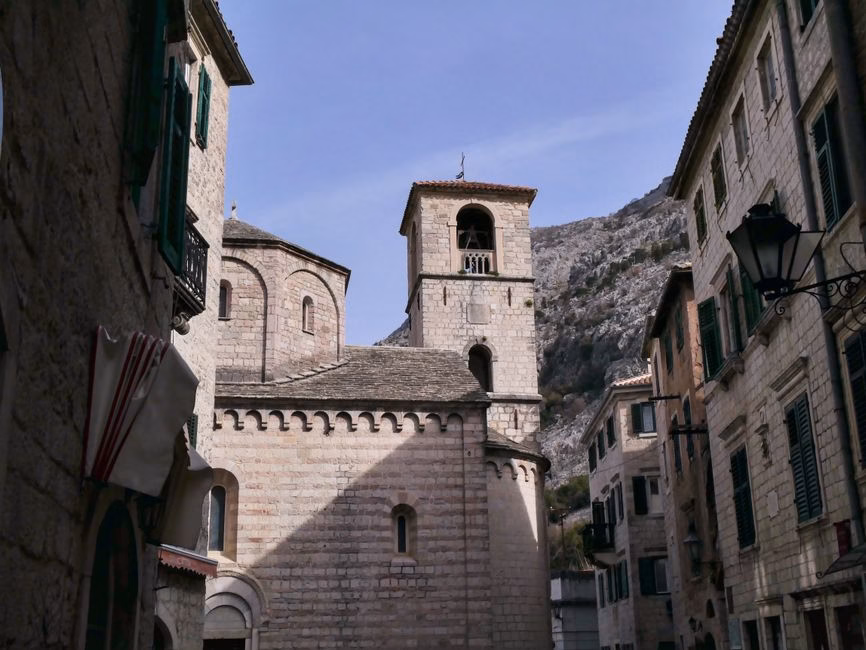 A picturesque view of a church in Kotor's old town with stone buildings and mountains.
