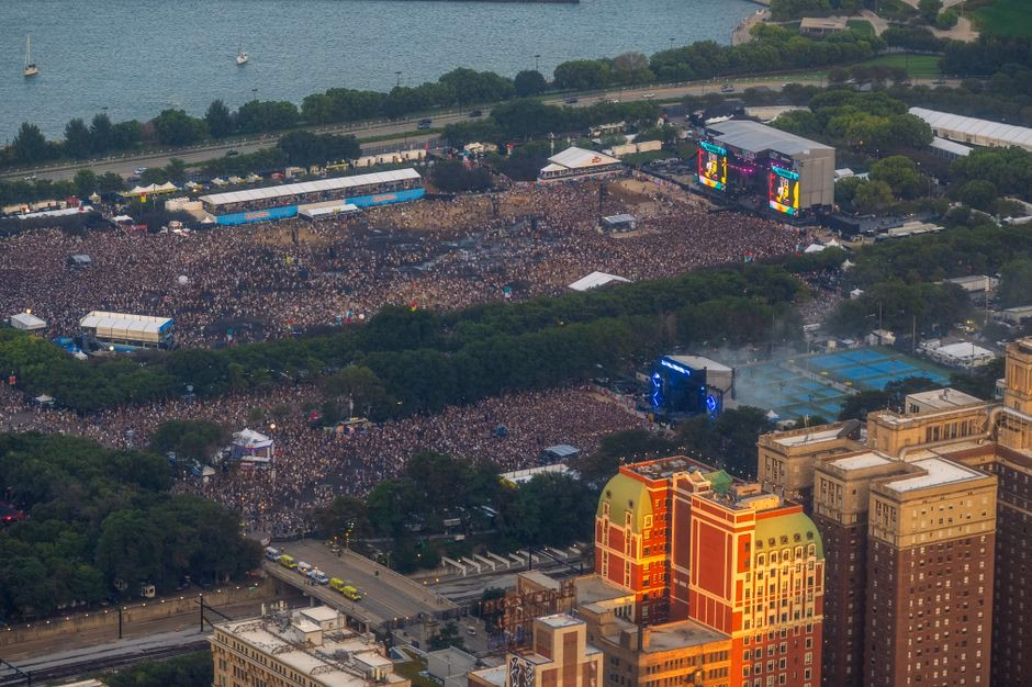 Aerial shot of a vibrant outdoor music festival with a large crowd and stage.