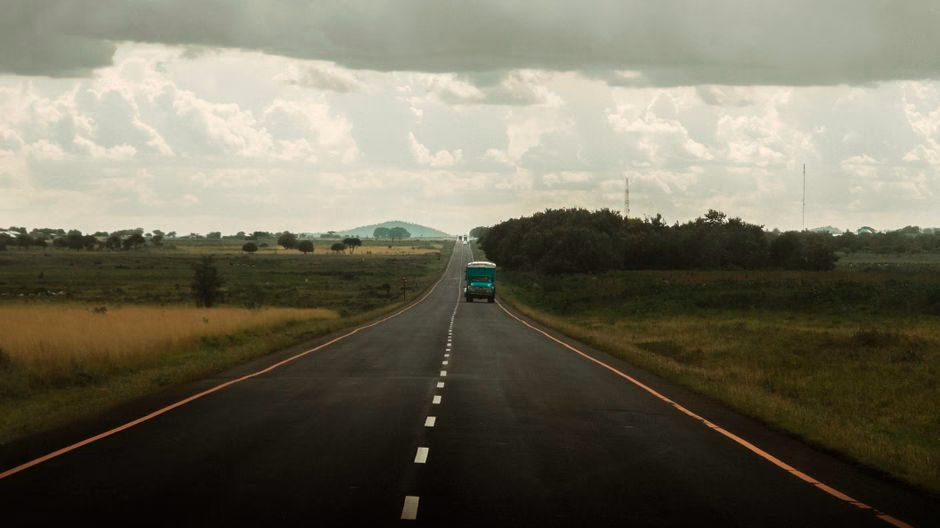 A scenic open road in Tanzania with a lone truck under a cloudy sky, capturing the essence of African travel.