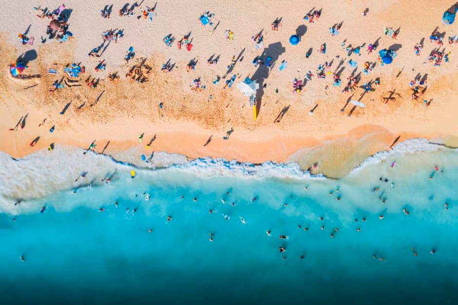 Aerial view of a crowded beach with turquoise waters and sunbathers enjoying a sunny day.